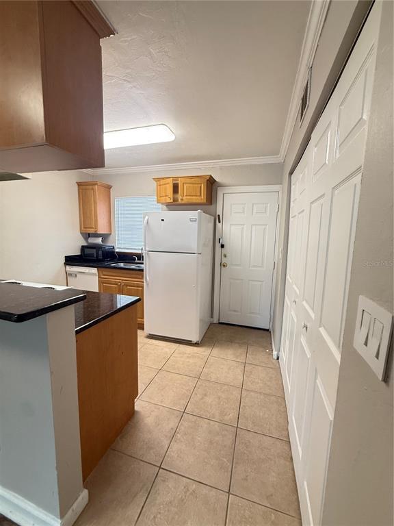 A kitchen features light-colored tile flooring, wood cabinets, a white refrigerator, and a white door — 630 SW 10TH LANE UNIT 2, GAINESVILLE, FL