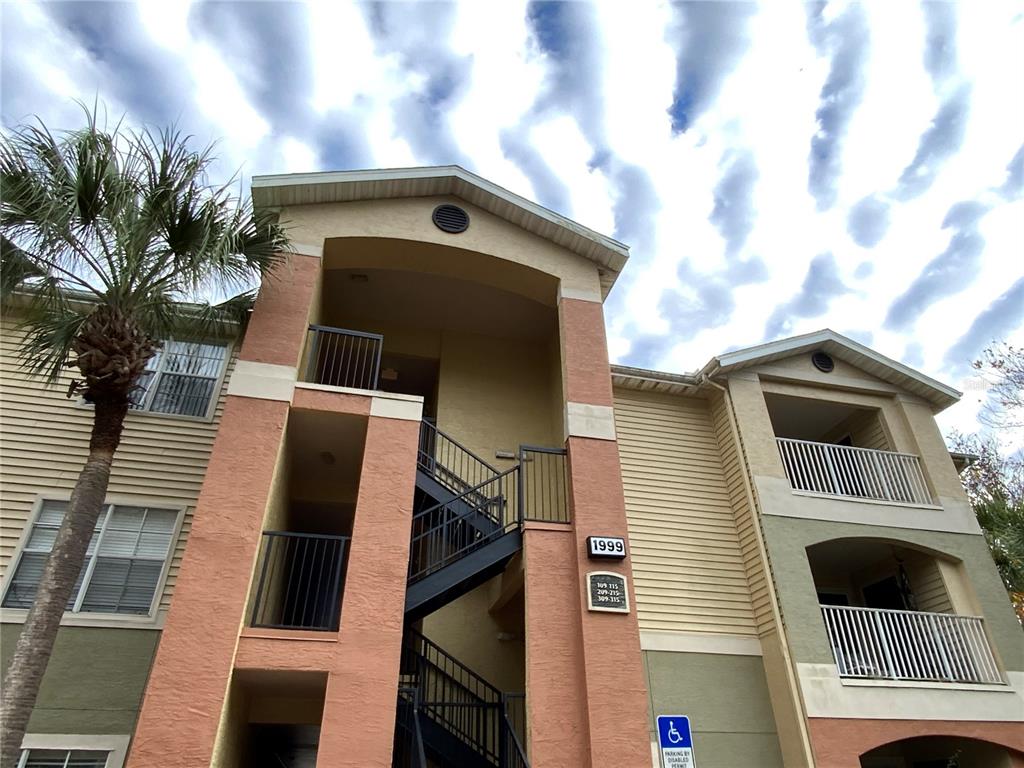 An exterior view of a multi-story apartment building with a staircase and a palm tree — 1999 SUMMER CLUB DRIVE UNIT 313, OVIEDO, FL