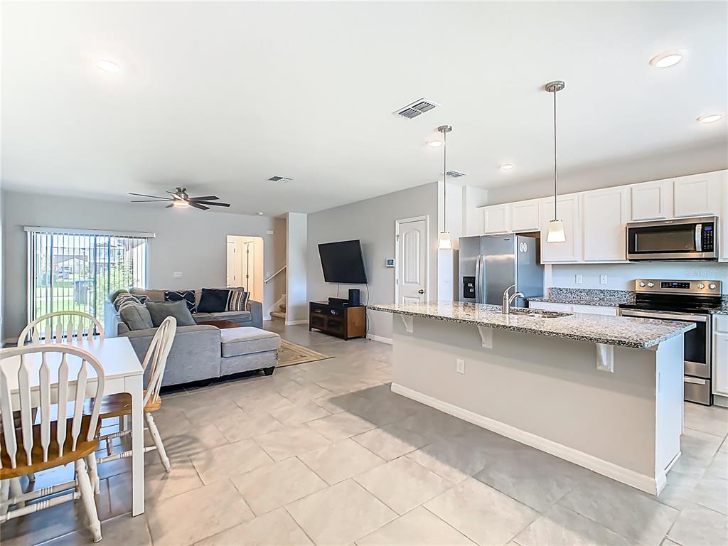 An open-concept living room and kitchen featuring tile flooring, white cabinetry, and granite countertops — 13158 BOUNTY AVENUE, WINTER GARDEN, FL