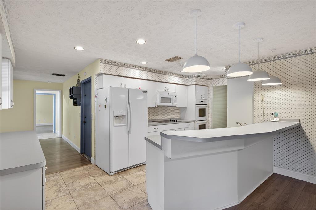 A kitchen features white cabinetry, a breakfast bar, pendant lighting, and patterned wallpaper — 901 W RIVER DRIVE, TEMPLE TERRACE, FL