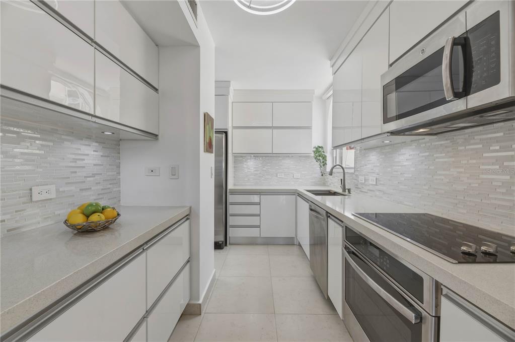 A modern galley kitchen features white glossy cabinets, stainless steel appliances, and light stone countertops — 16 CARRION COURT UNIT 24, SAN JUAN, PR