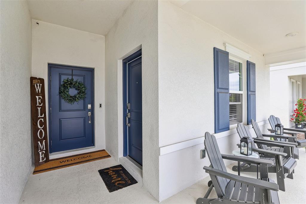 A covered porch features two blue doors, gray Adirondack chairs, and a welcome sign — 5671 WOOD BRIDGE PLACE, ST CLOUD, FL
