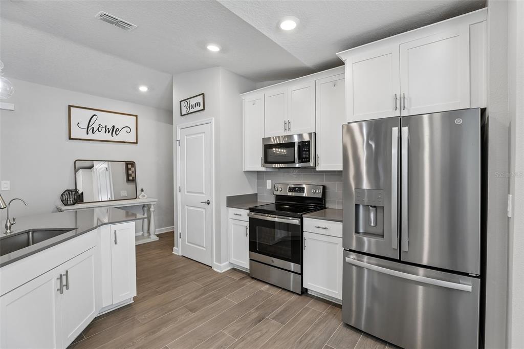 A modern kitchen features white cabinets, stainless steel appliances, and wood-look tile flooring — 5671 WOOD BRIDGE PLACE, ST CLOUD, FL