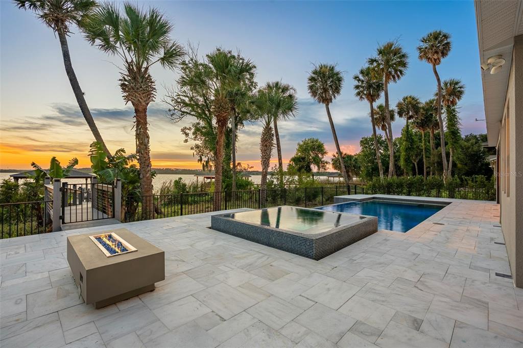 A patio features a fire pit, a raised spa, and a pool overlooking a lake — 1144 HULL ISLAND DRIVE, WINTER GARDEN, FL