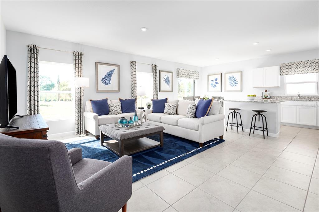 A bright open-concept living room features a kitchen island, tiled floors, and blue accent decor — 4826 RIVER BIRCH BEND, LAKELAND, FL