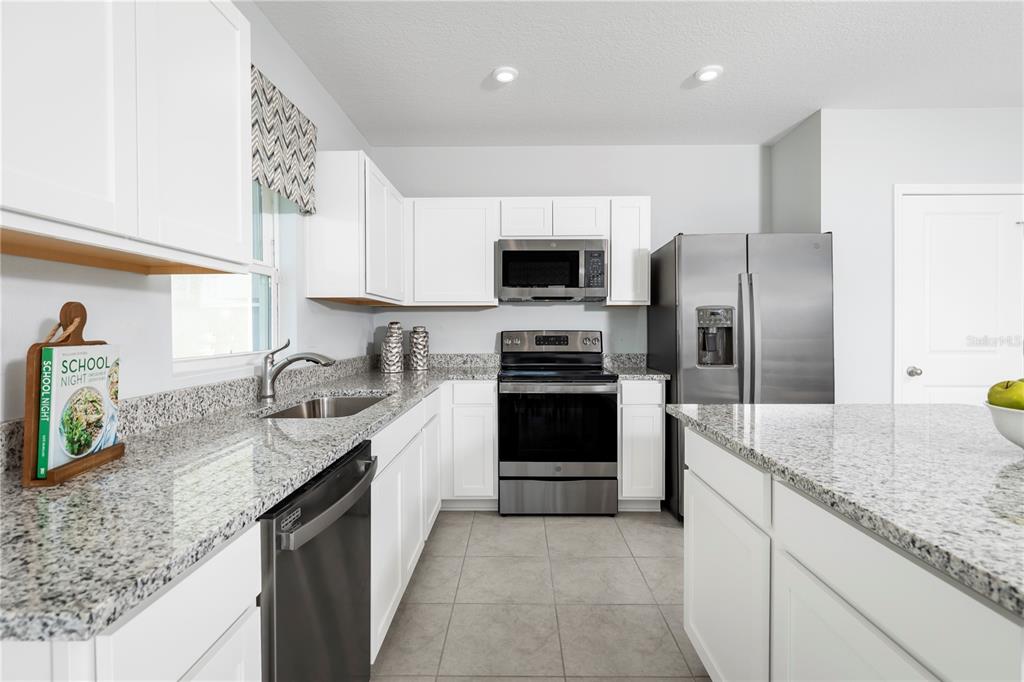 A kitchen with white cabinets, granite countertops, stainless steel appliances, and tile flooring — 4826 RIVER BIRCH BEND, LAKELAND, FL
