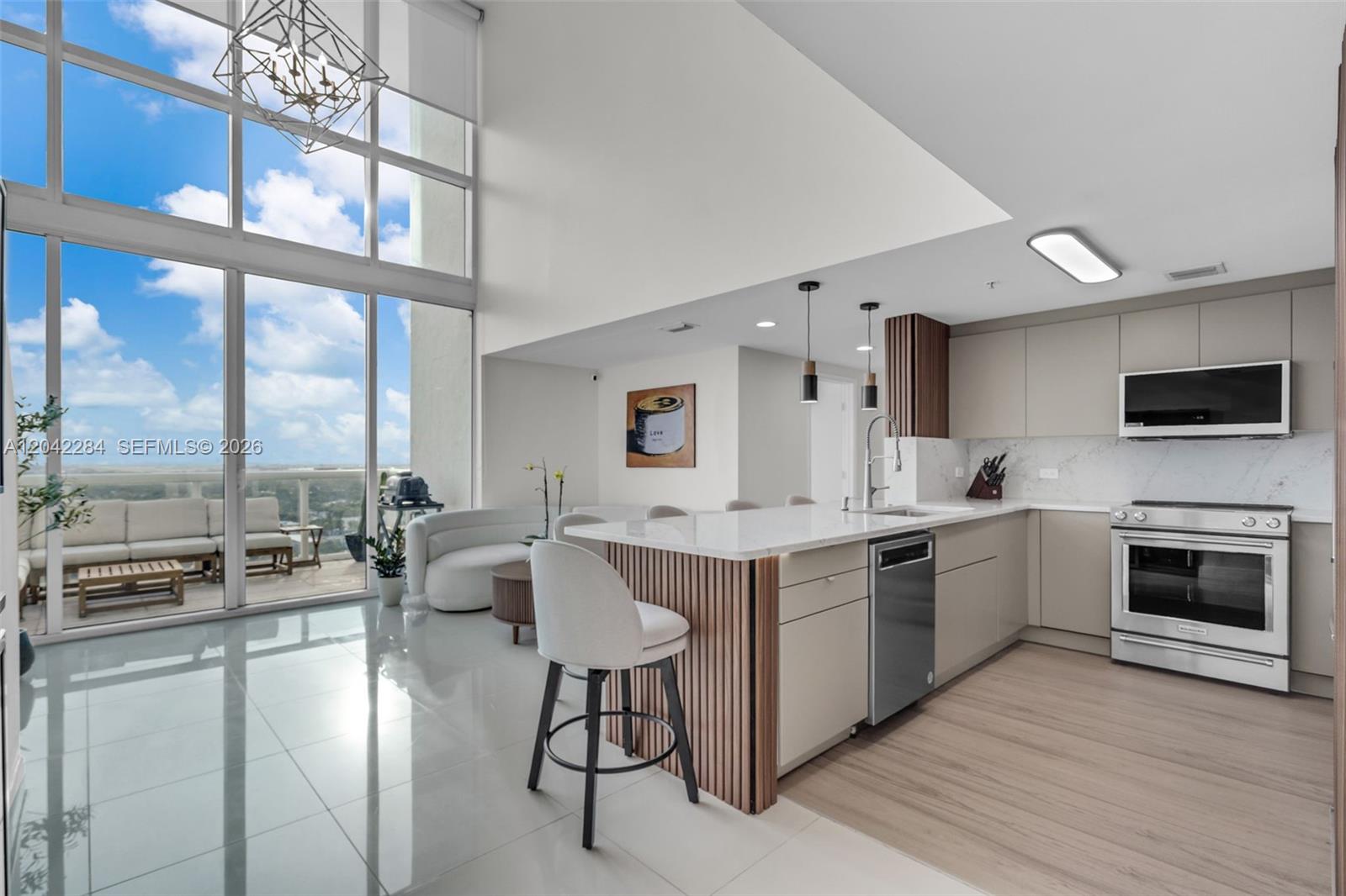 A modern kitchen with a slatted island, stainless steel appliances, and floor-to-ceiling windows overlooking a balcony — 1861 NW S River Dr, Miami FL 33125, MIAMI, FL