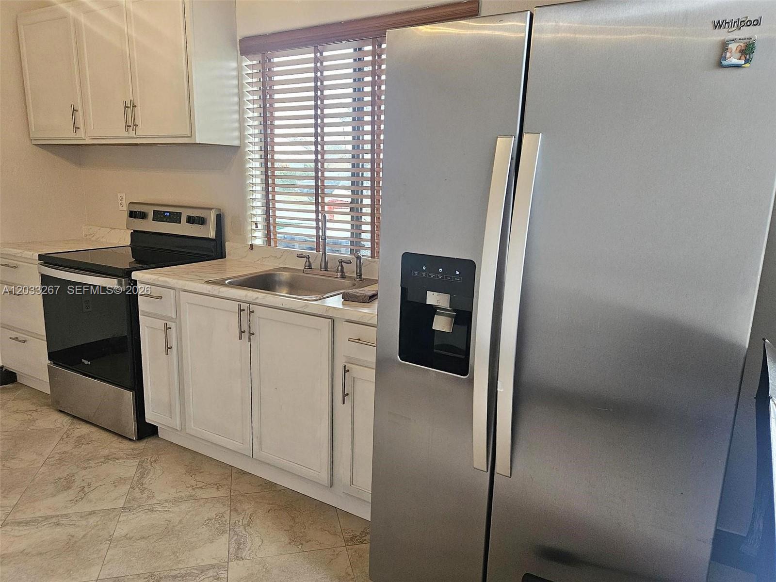 A kitchen features white cabinets, stainless steel appliances, a sink, and light-colored tile flooring — 12975 SW 189th St # 1, Miami FL 33177, MIAMI, FL