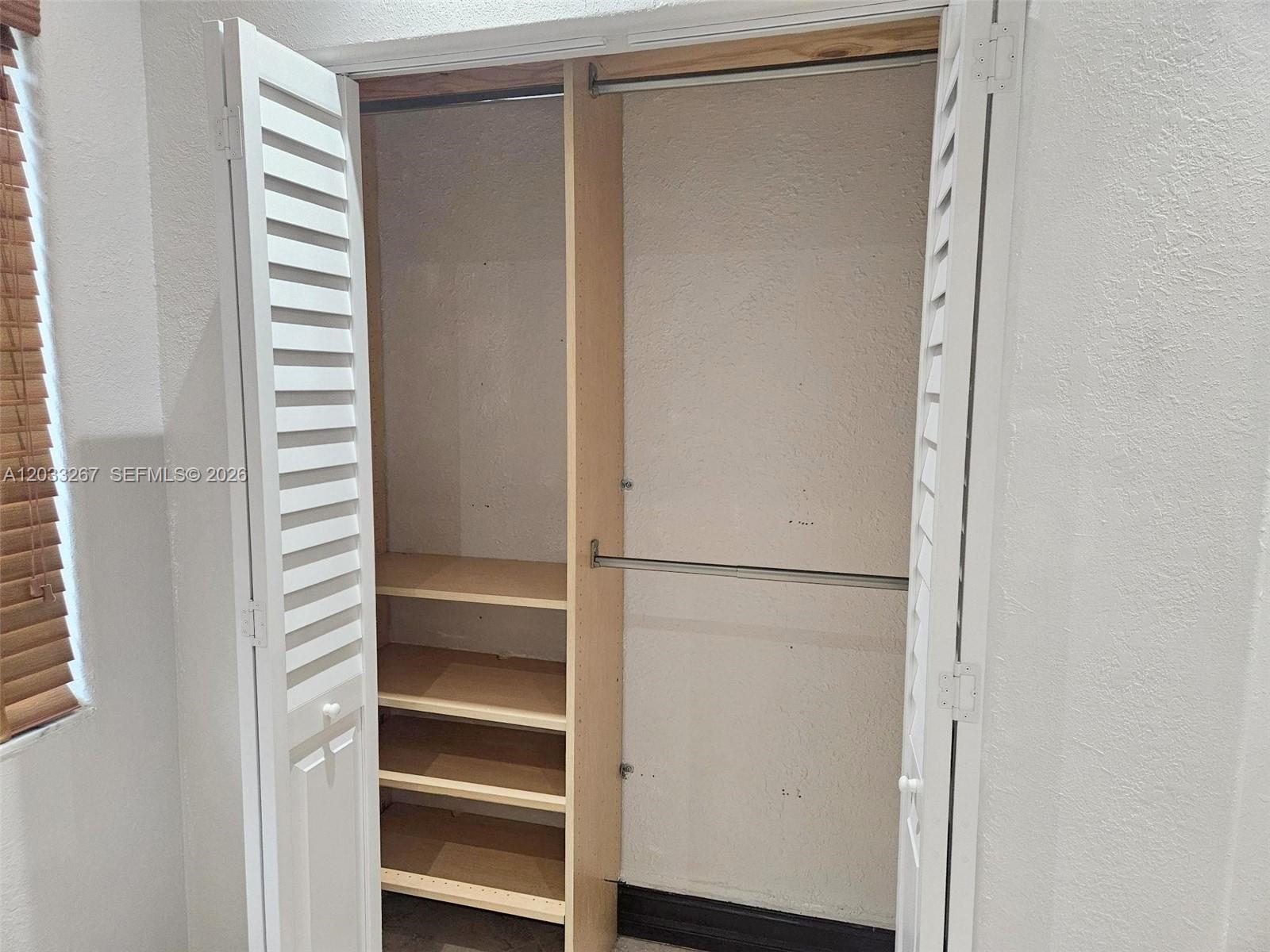 An open closet features white louvered doors, a central divider, shelving, and a hanging rod — 12975 SW 189th St # 1, Miami FL 33177, MIAMI, FL