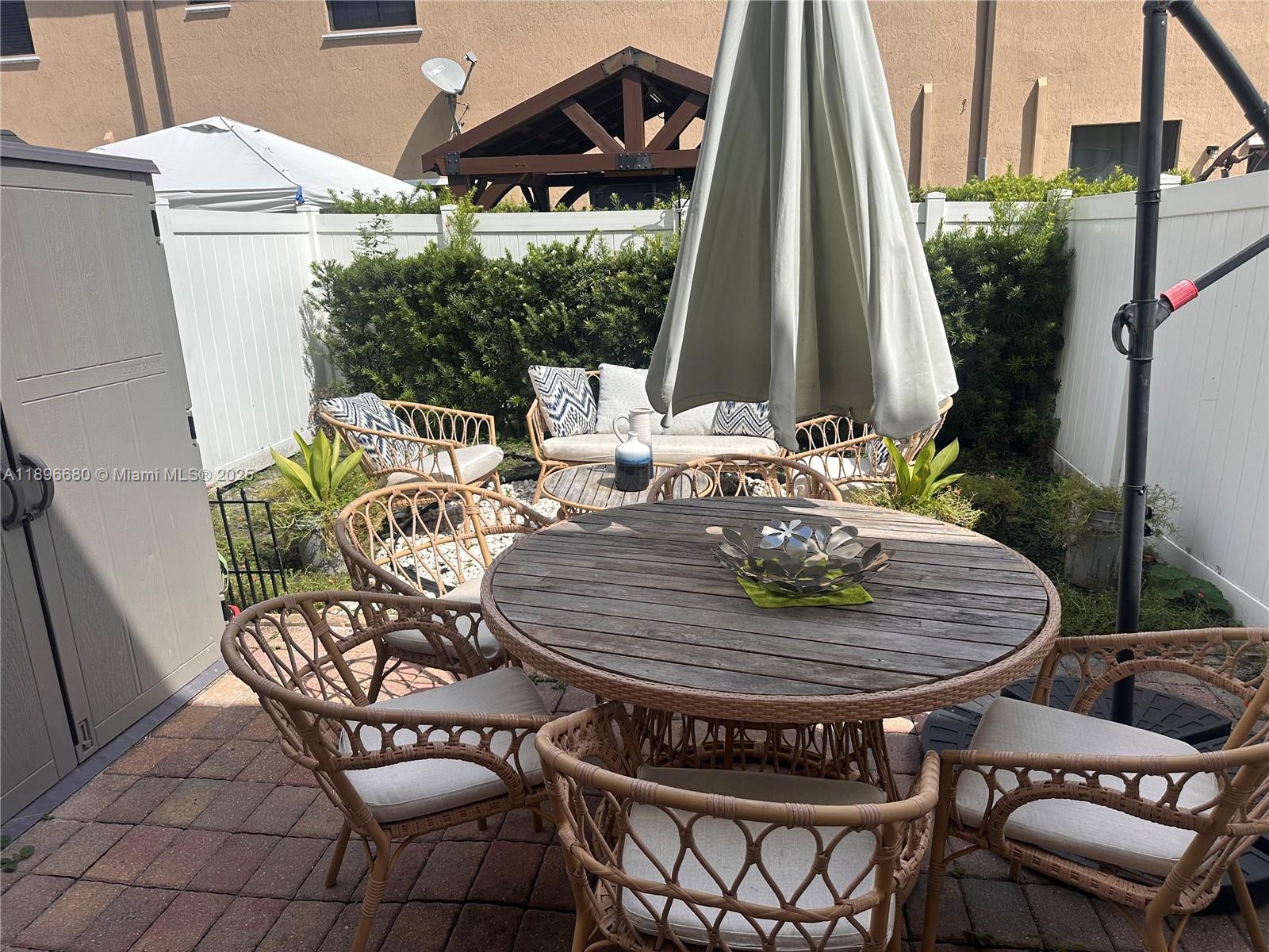 A patio features a round wooden table, wicker chairs, and a closed umbrella — 8867 W 35th Way, Hialeah FL 33018, HIALEAH, FL