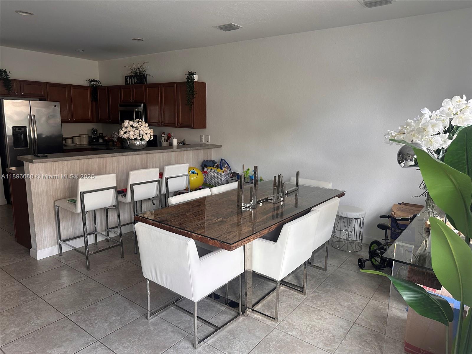 A dining area with a glass-topped table and white chairs sits adjacent to a kitchen — 8867 W 35th Way, Hialeah FL 33018, HIALEAH, FL