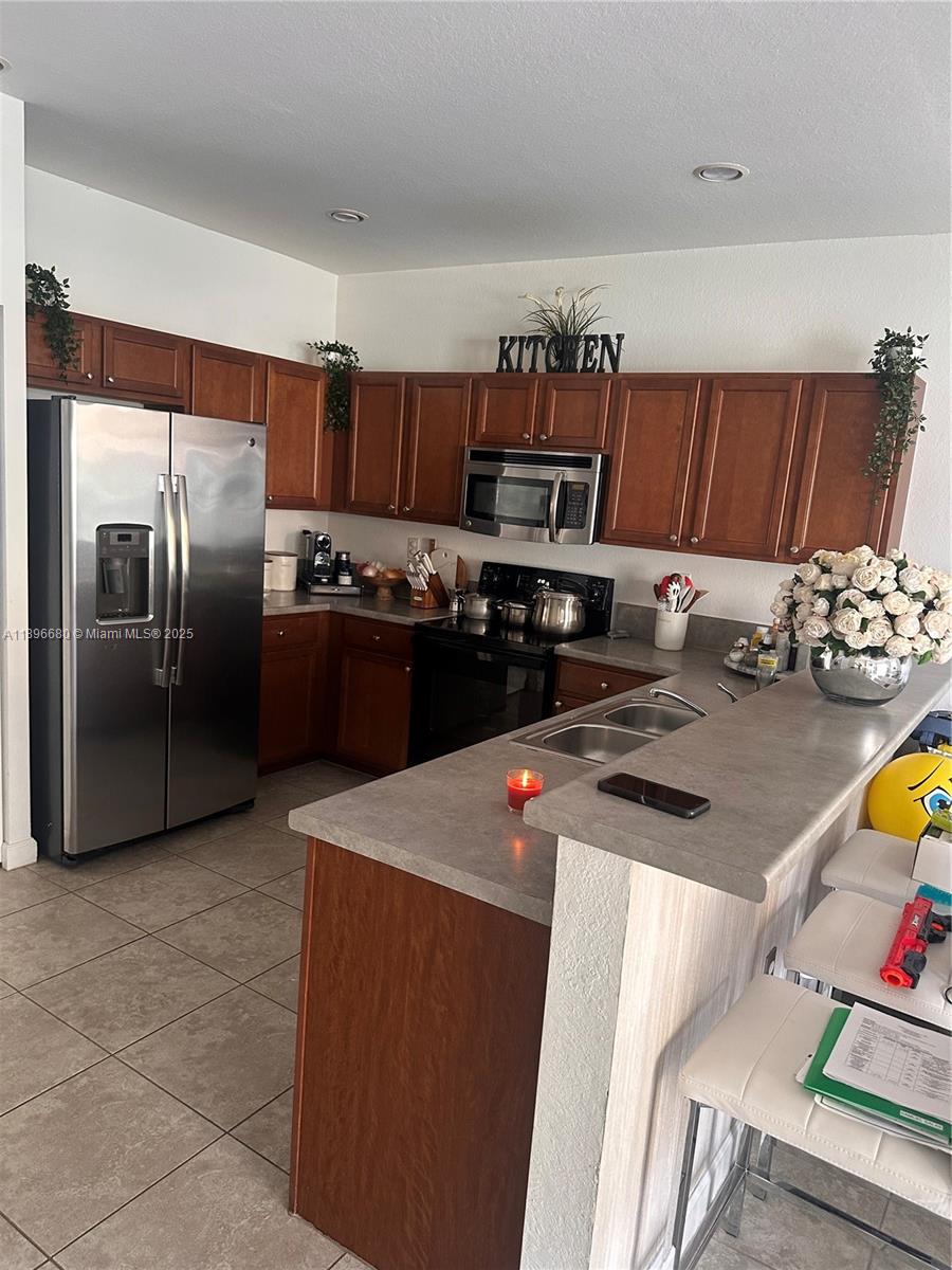 A kitchen features wood cabinets, stainless steel appliances, and a gray countertop breakfast bar — 8867 W 35th Way, Hialeah FL 33018, HIALEAH, FL