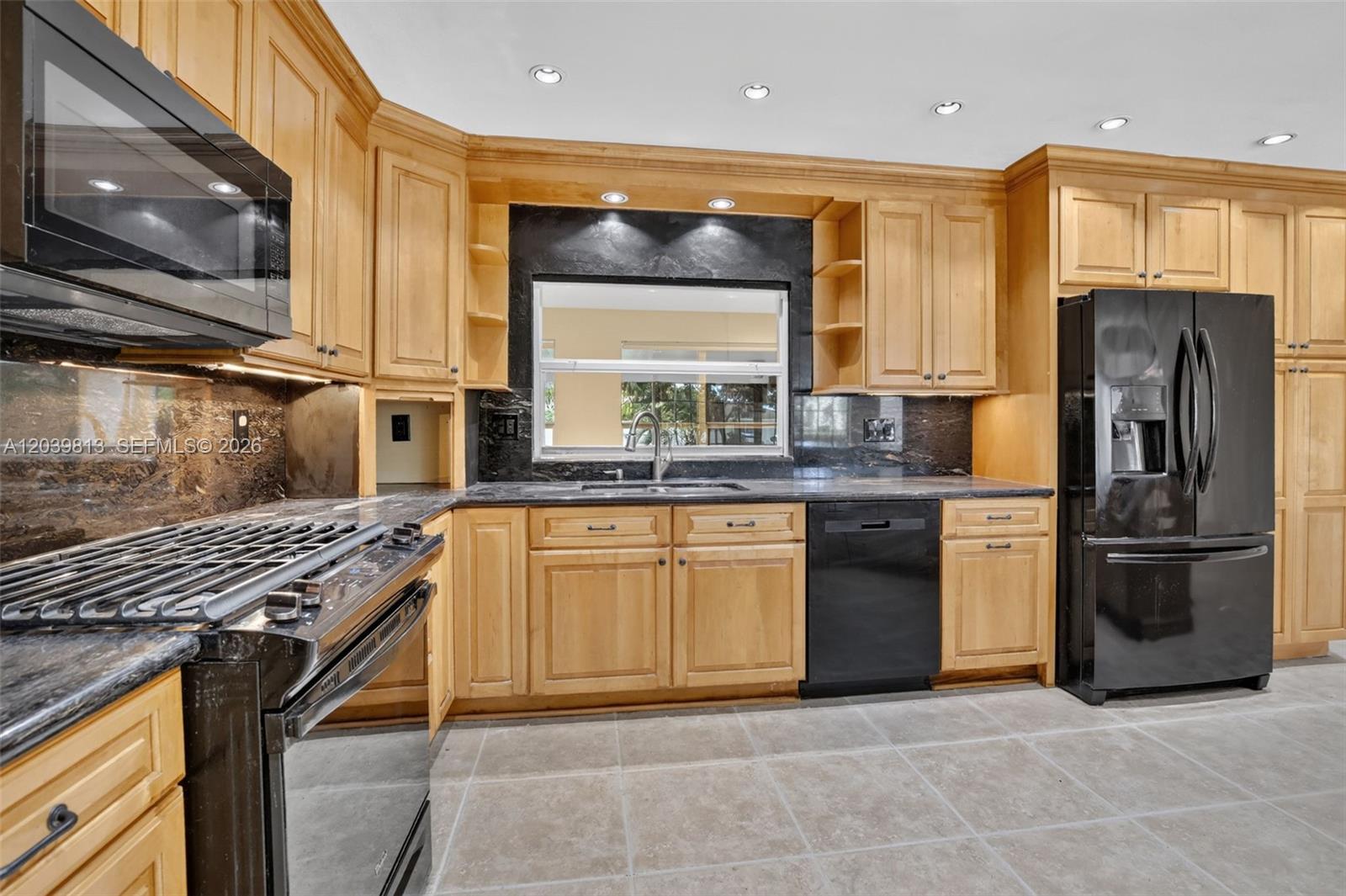 A kitchen features light wood cabinets, black appliances, and dark stone countertops — 5511 Taylor St, Hollywood FL 33021, HOLLYWOOD, FL