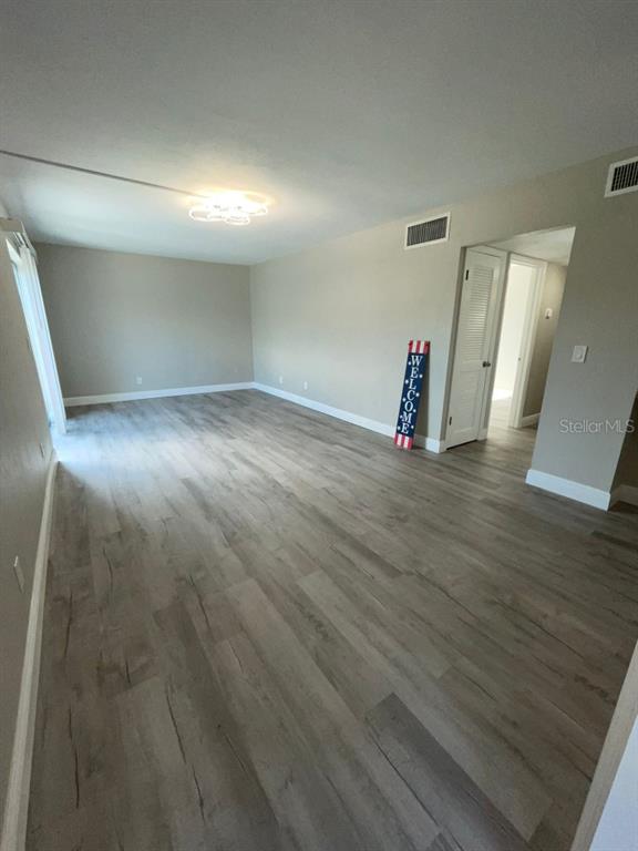 An empty room features light-colored wood-look flooring, beige walls, and a ceiling light fixture — 1799 N HIGHLAND AVENUE UNIT 172, CLEARWATER, FL