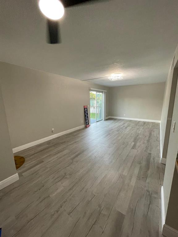An empty living room features light gray wood-look flooring, neutral walls, and a sliding glass door — 1799 N HIGHLAND AVENUE UNIT 172, CLEARWATER, FL