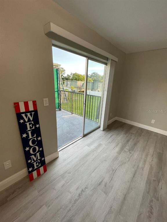 A room with light wood-look flooring, a sliding glass door, and a patriotic welcome sign — 1799 N HIGHLAND AVENUE UNIT 172, CLEARWATER, FL