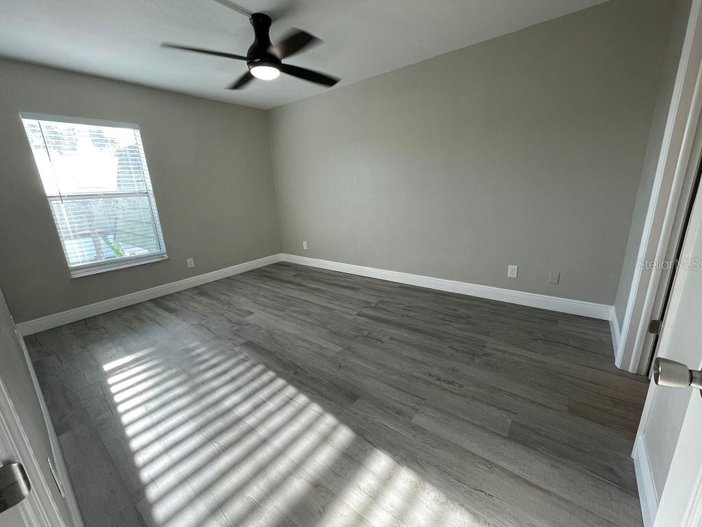 An empty bedroom features gray wood-look flooring, light gray walls, and a ceiling fan — 1799 N HIGHLAND AVENUE UNIT 172, CLEARWATER, FL