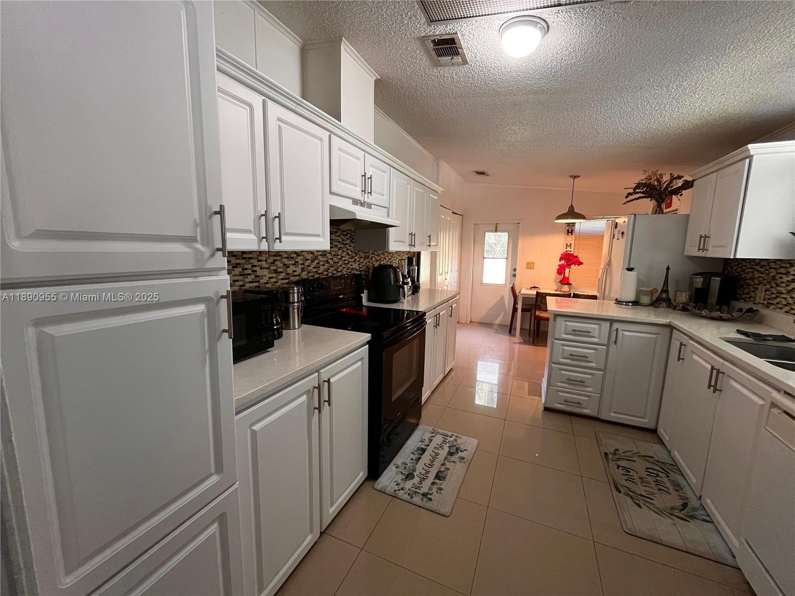 A kitchen features white cabinetry, black appliances, light countertops, and tiled flooring — 909 Sw 131 Way, Davie FL 33325, DAVIE, FL