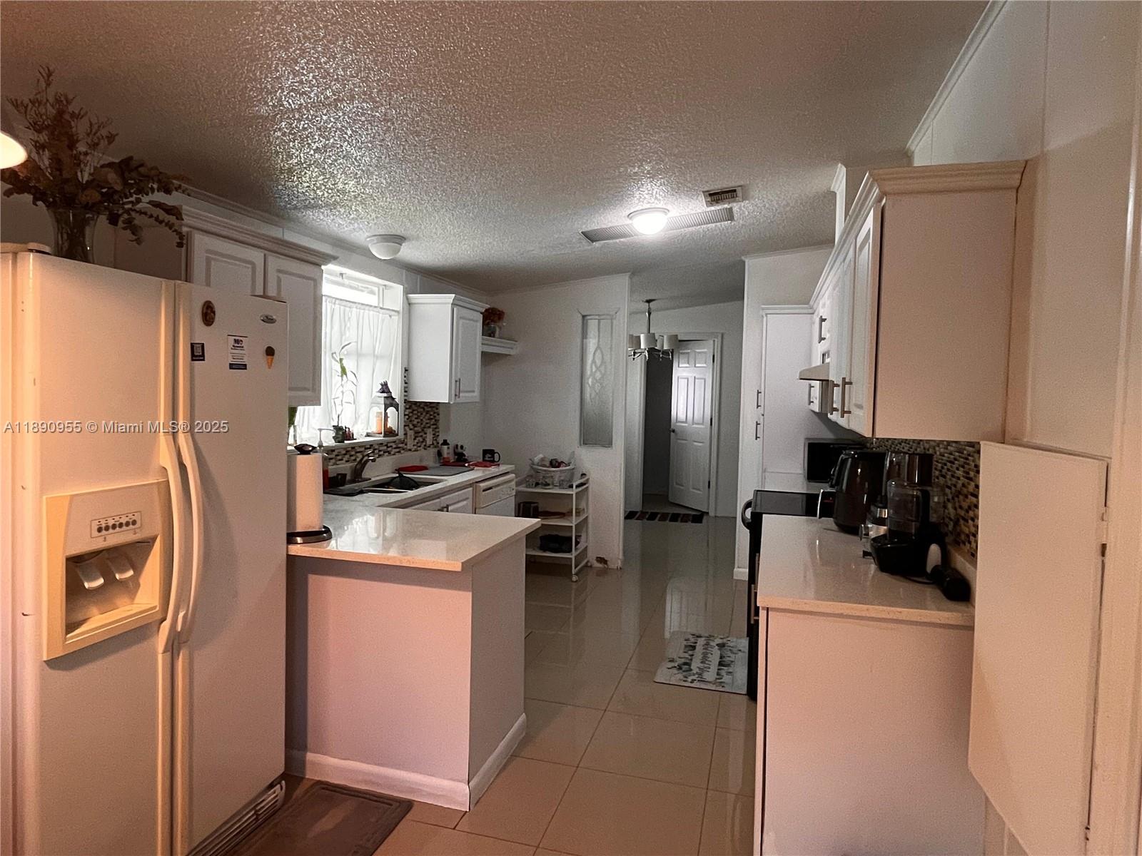 A kitchen features white cabinetry, light countertops, tile flooring, and a refrigerator — 909 Sw 131 Way, Davie FL 33325, DAVIE, FL