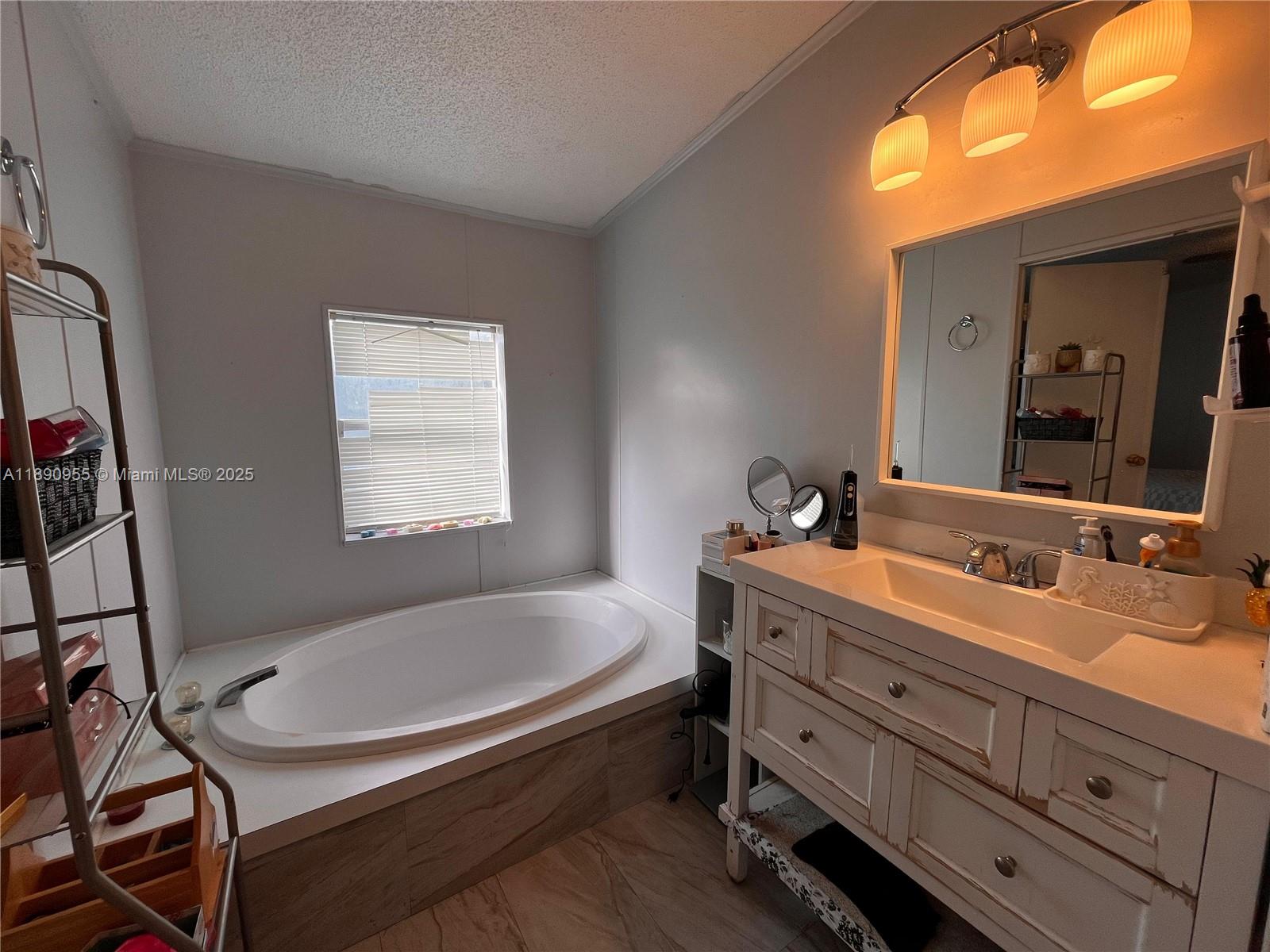 A bathroom features a white soaking tub, a distressed wood vanity, and a wall mirror — 909 Sw 131 Way, Davie FL 33325, DAVIE, FL