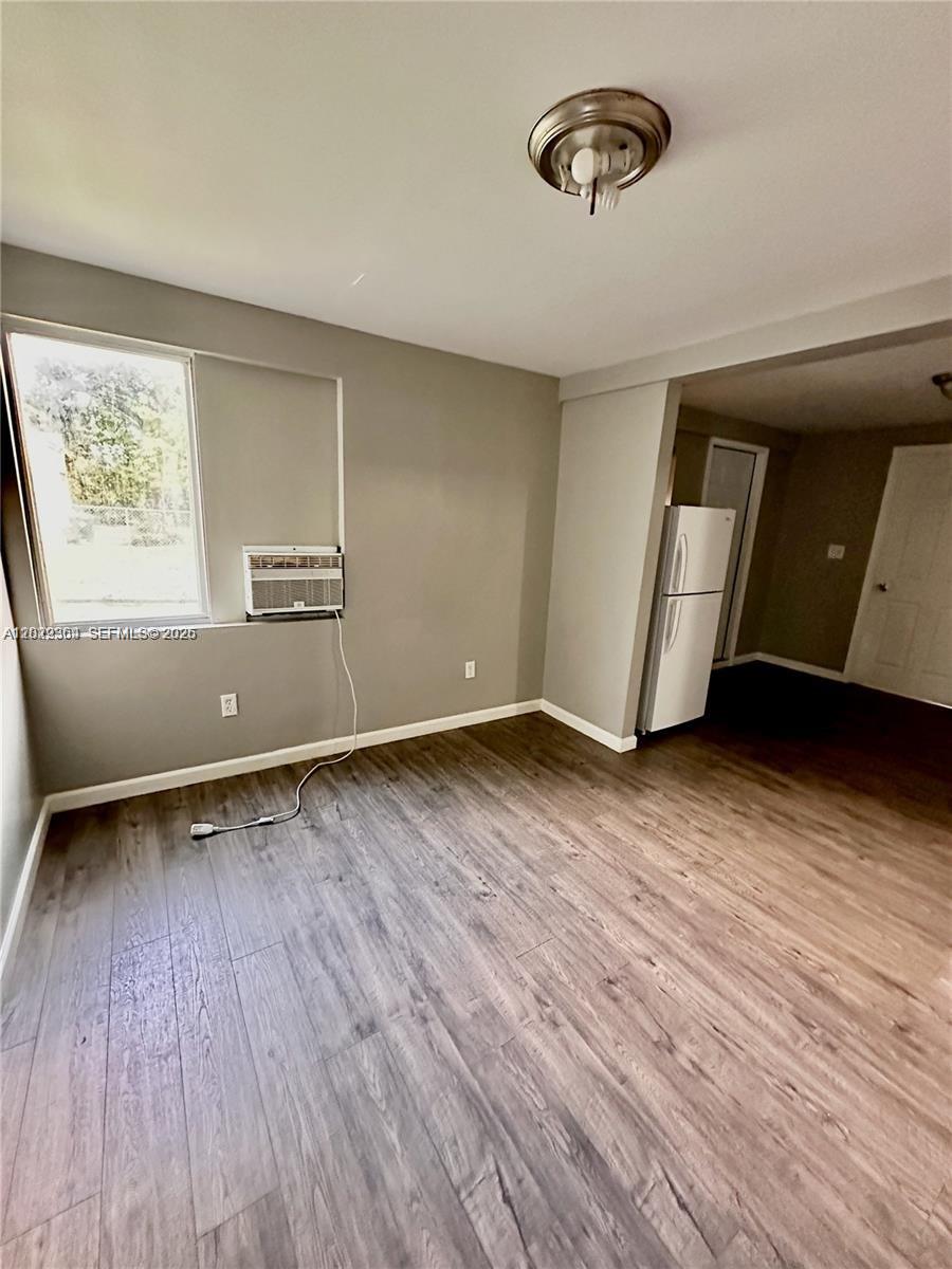A room with wood-look flooring, a window air conditioning unit, and an adjacent kitchen area — 6326 NW 4th Ave # 3, Miami FL 33150, MIAMI, FL