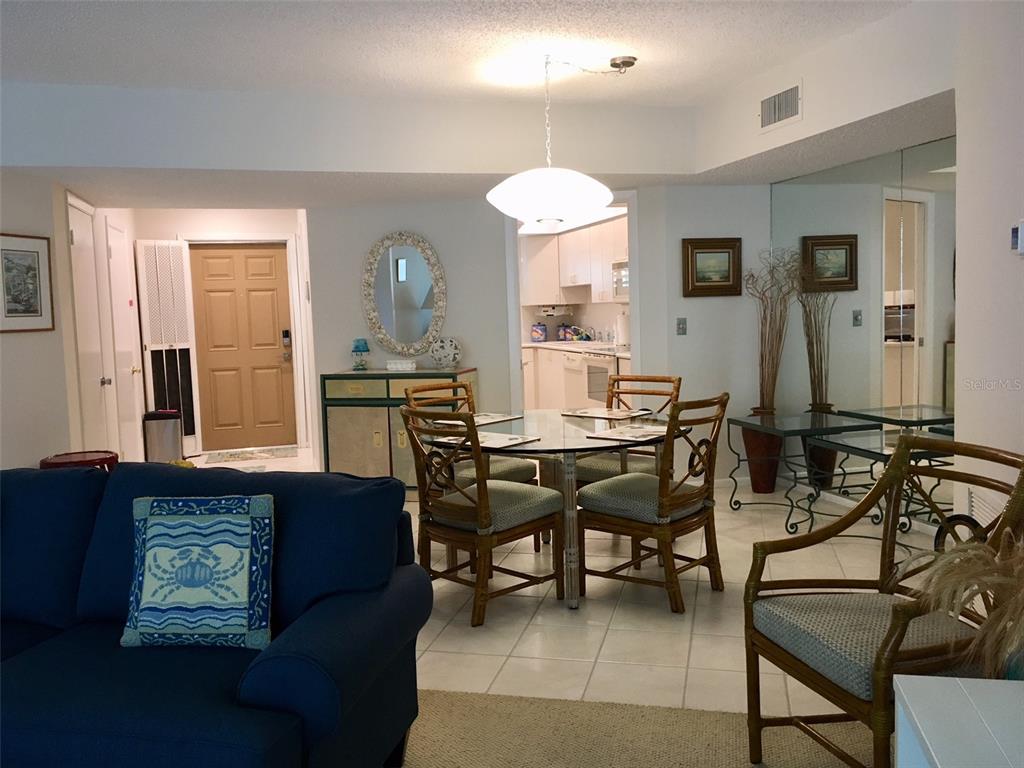 A dining area with a glass table and rattan chairs sits beside a blue sofa — 4825 GULF OF MEXICO DRIVE UNIT 201, LONGBOAT KEY, FL