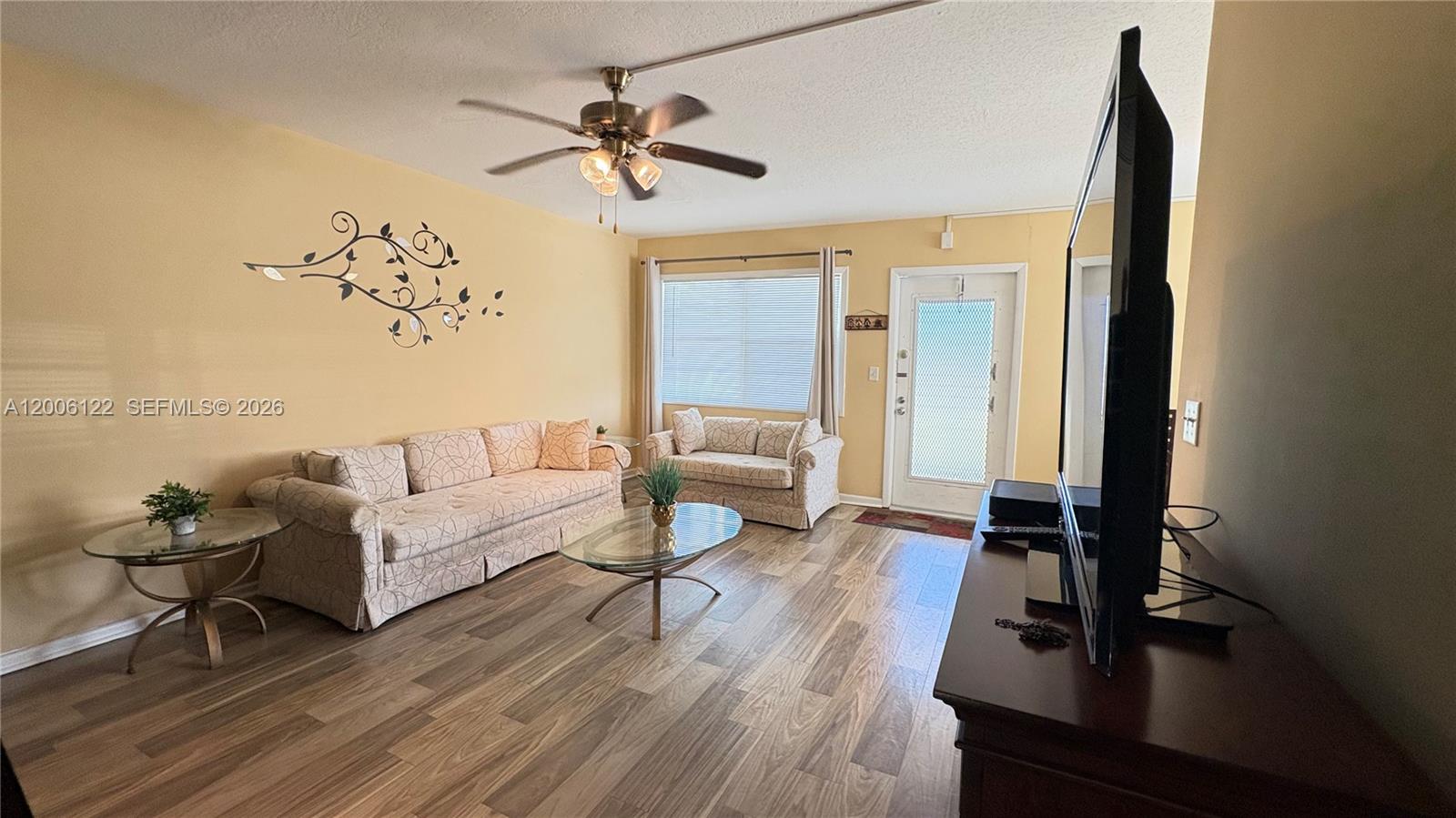 A living room features light-colored sofas, a glass coffee table, and wood-look flooring — 1044 Harwood D # D, Deerfield Beach FL 33442, DEERFIELD BEACH, FL