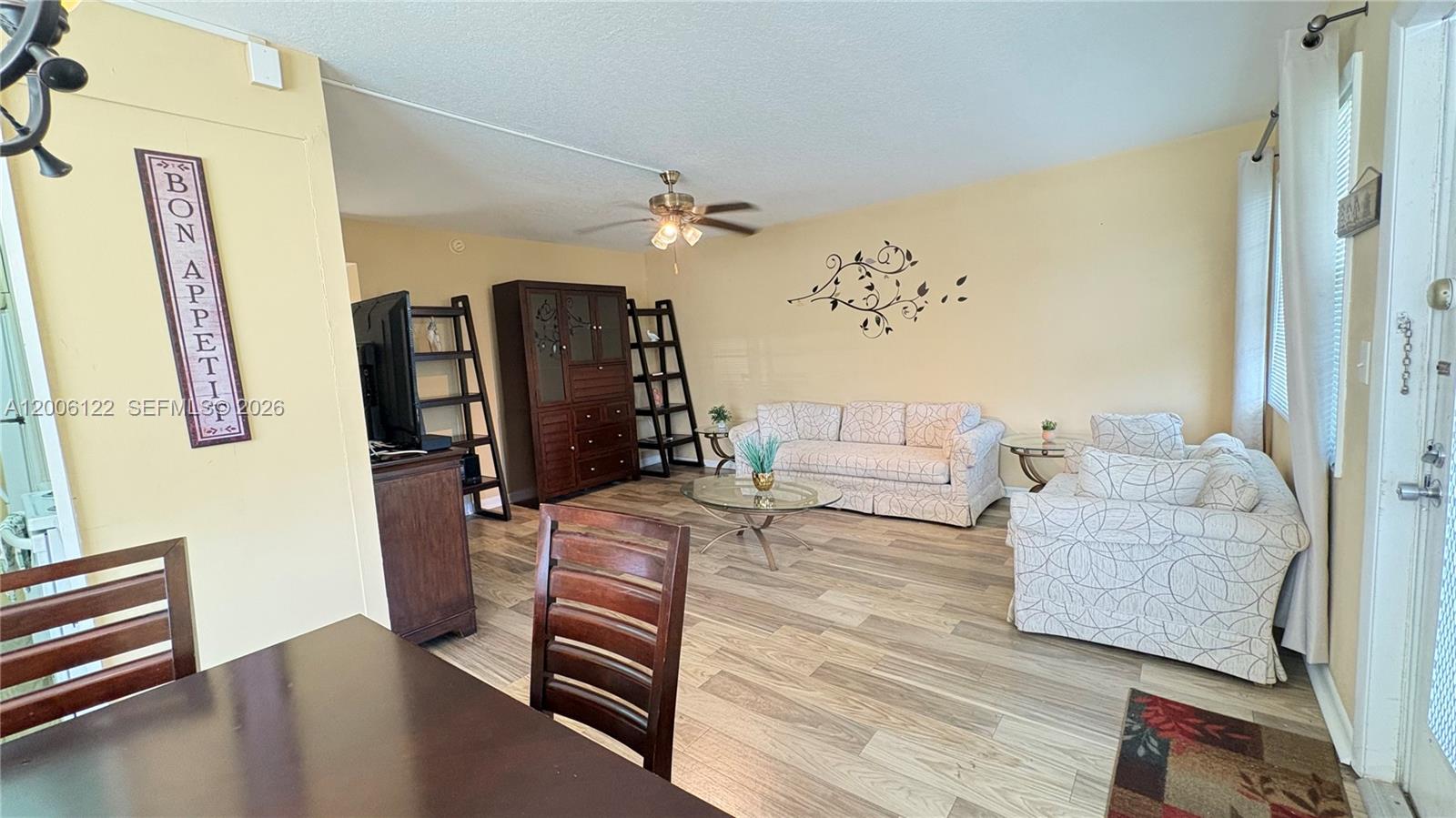A living room features light-colored walls, wood-look flooring, a ceiling fan, and patterned furniture — 1044 Harwood D # D, Deerfield Beach FL 33442, DEERFIELD BEACH, FL