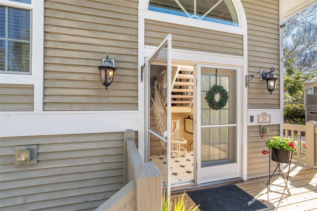 An exterior view of a house entrance with tan siding, a screen door, and stairs — 36 SEAWATCH DRIVE, BOCA GRANDE, FL