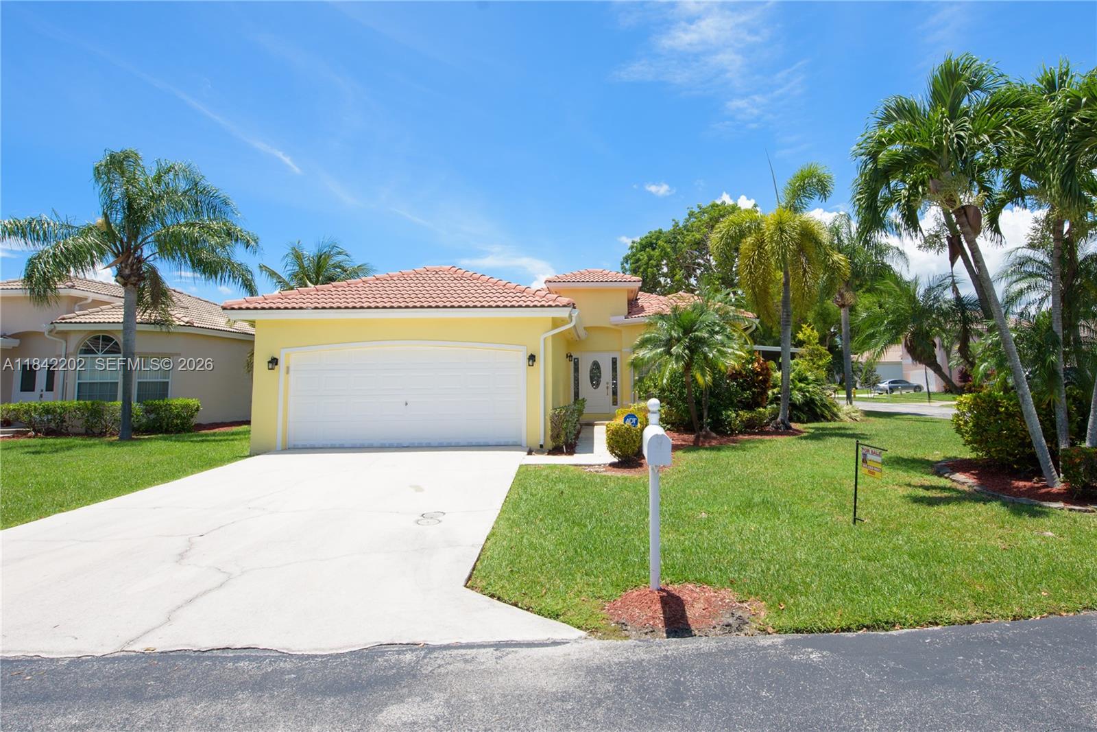 A yellow single-story house with a tile roof, two-car garage, and palm trees — 460 SE 24th Dr, Homestead FL 33033, HOMESTEAD, FL
