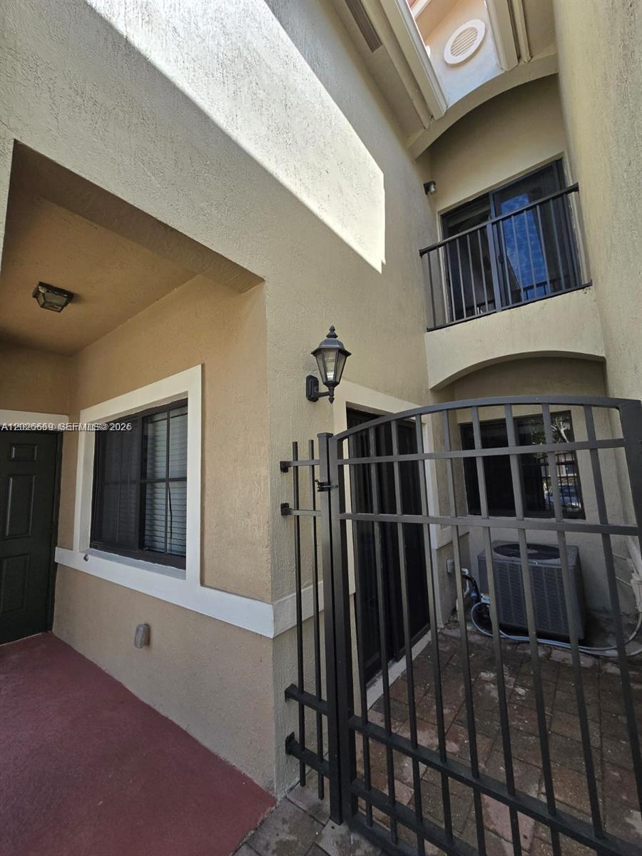 A gated patio area features a tan stucco exterior, a window, and an air conditioner — CUTLER BAY, FL