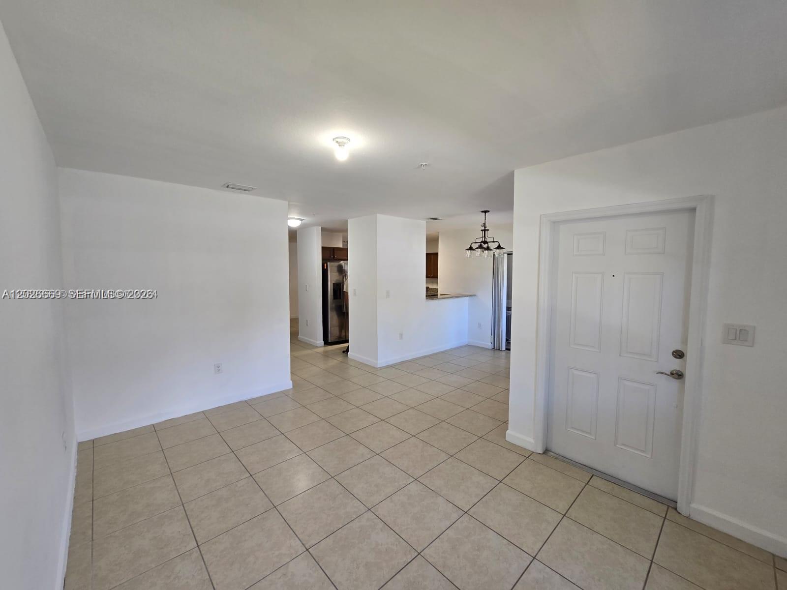 A bright, open-concept living area features white walls, tile flooring, and an adjacent kitchen — CUTLER BAY, FL