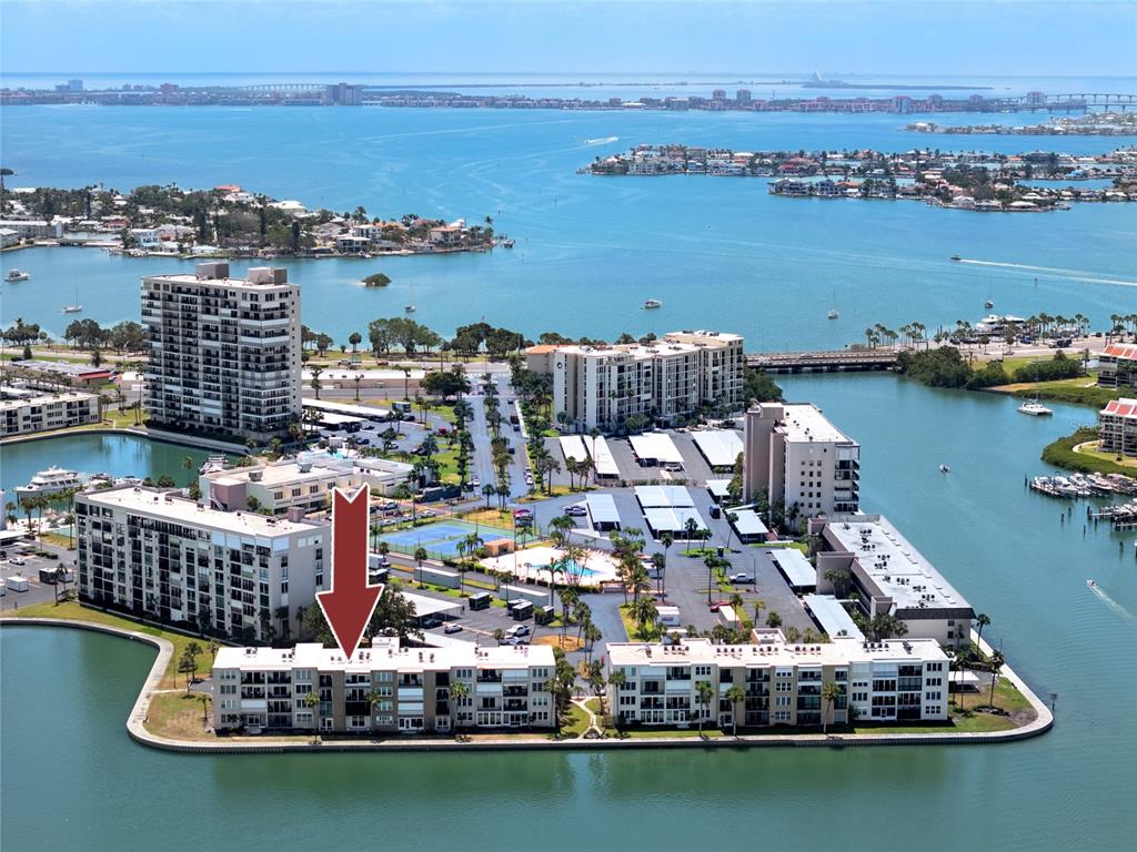 An aerial view shows a waterfront condominium complex with a red arrow pointing to a unit — 7910 SUN ISLAND DRIVE S UNIT 203, SOUTH PASADENA, FL
