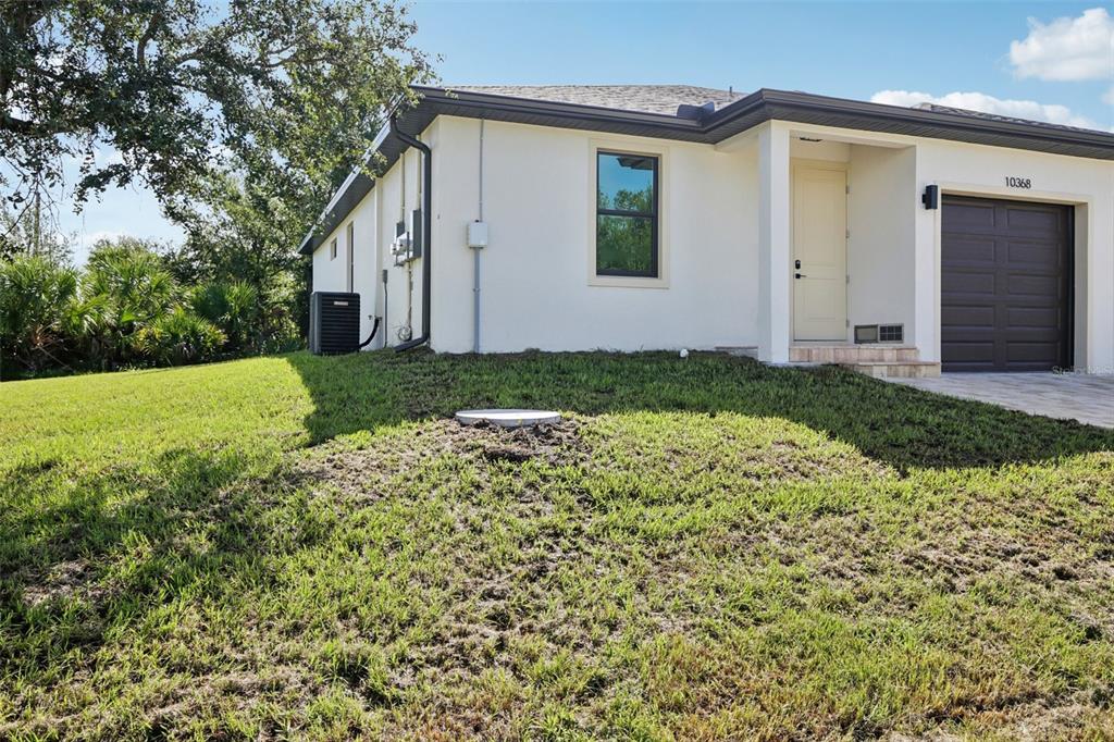 A side view of a light-colored house with a dark garage door and grassy yard — 10368 PORT EVERGLADES STREET, PORT CHARLOTTE, FL