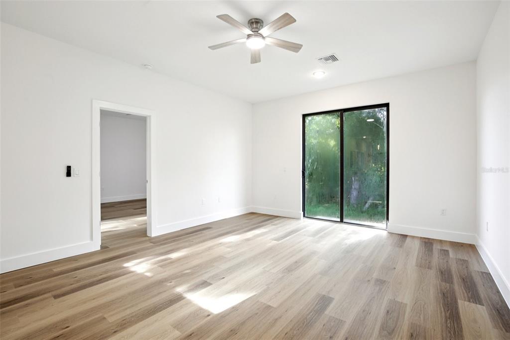 A bright bedroom features light wood-look flooring, a ceiling fan, and sliding glass patio doors — 10368 PORT EVERGLADES STREET, PORT CHARLOTTE, FL