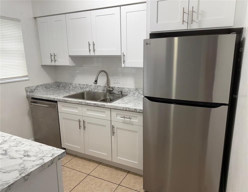 A kitchen features white cabinets, marble-patterned countertops, stainless steel appliances, and tile flooring — 5325 CURRY FORD ROAD UNIT G202, ORLANDO, FL