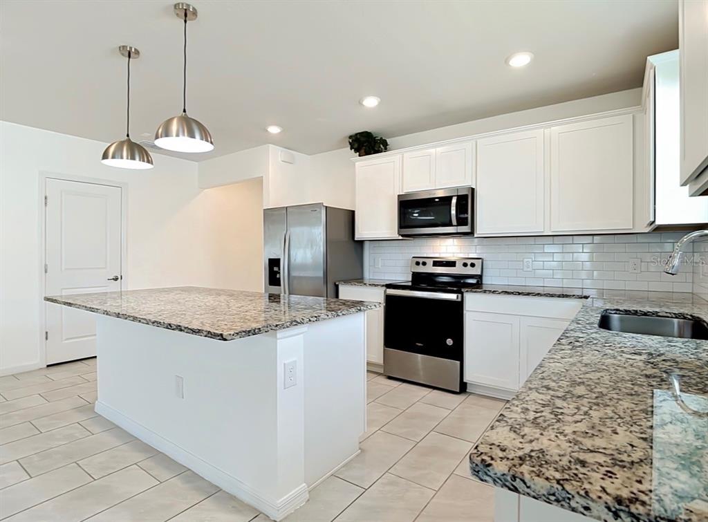 A kitchen features white cabinets, granite countertops, stainless steel appliances, and a central island — 1059 MICHELANGELO LANE, WINTER HAVEN, FL