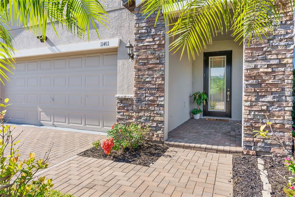A residential exterior features a stone-accented entryway, a paved walkway, and a tan garage door — 11411 CHILLY WATER COURT, RIVERVIEW, FL