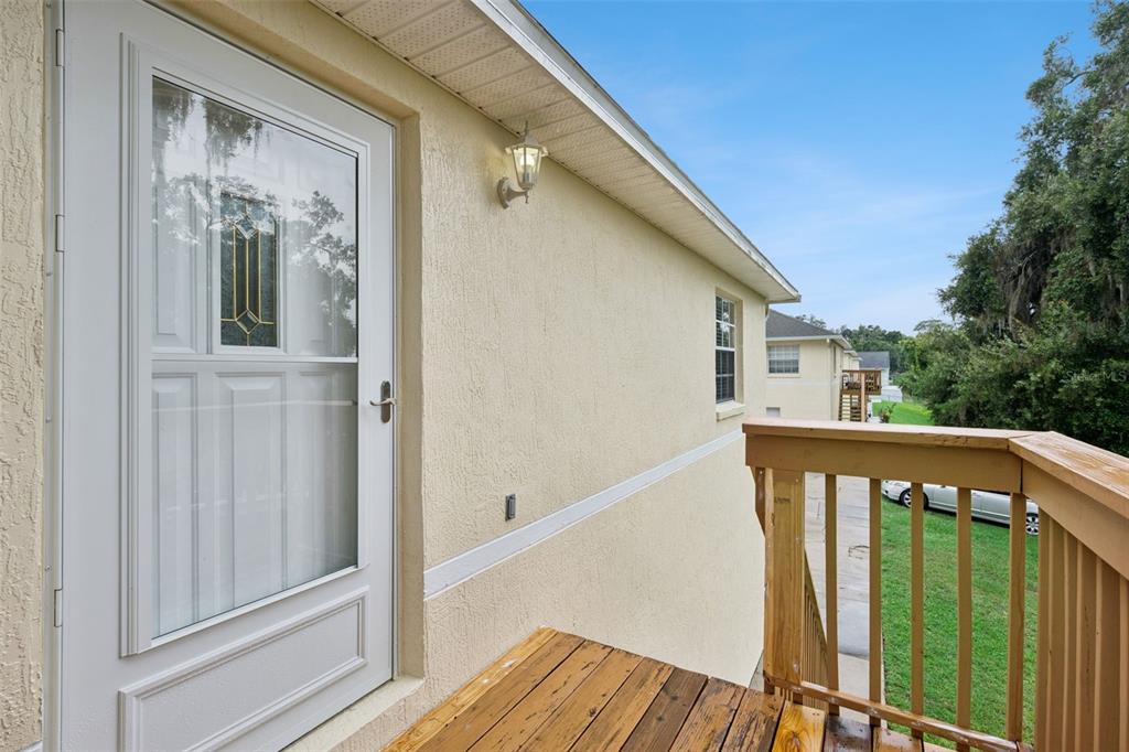 A wooden deck with a railing leads to a white storm door on a house exterior — 180 E MINNEHAHA AVENUE, CLERMONT, FL