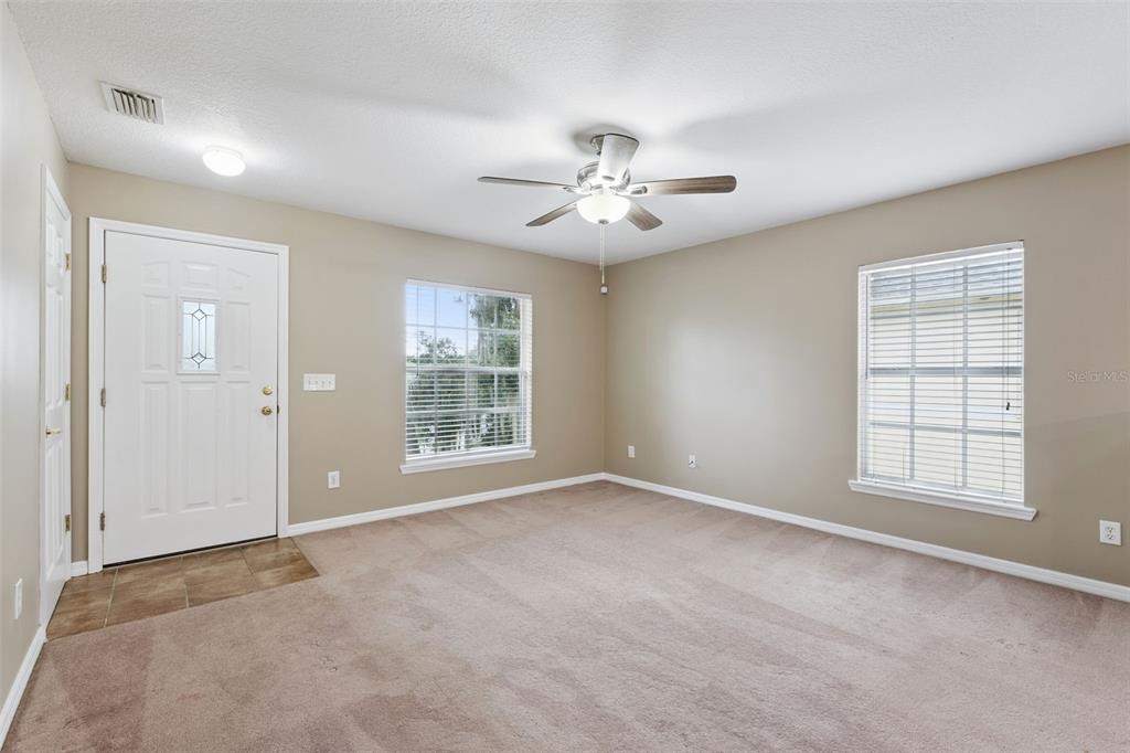 A living room with beige walls, tan carpeting, a ceiling fan, and two windows — 180 E MINNEHAHA AVENUE, CLERMONT, FL