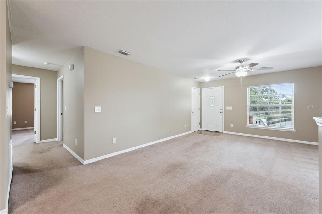A carpeted living room features a ceiling fan, a front door, and a window — 180 E MINNEHAHA AVENUE, CLERMONT, FL