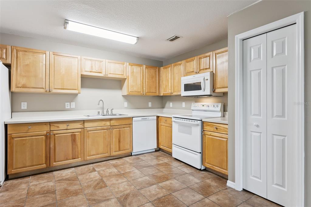 A kitchen with light wood cabinets, white appliances, a white countertop, and brown tile flooring — 180 E MINNEHAHA AVENUE, CLERMONT, FL
