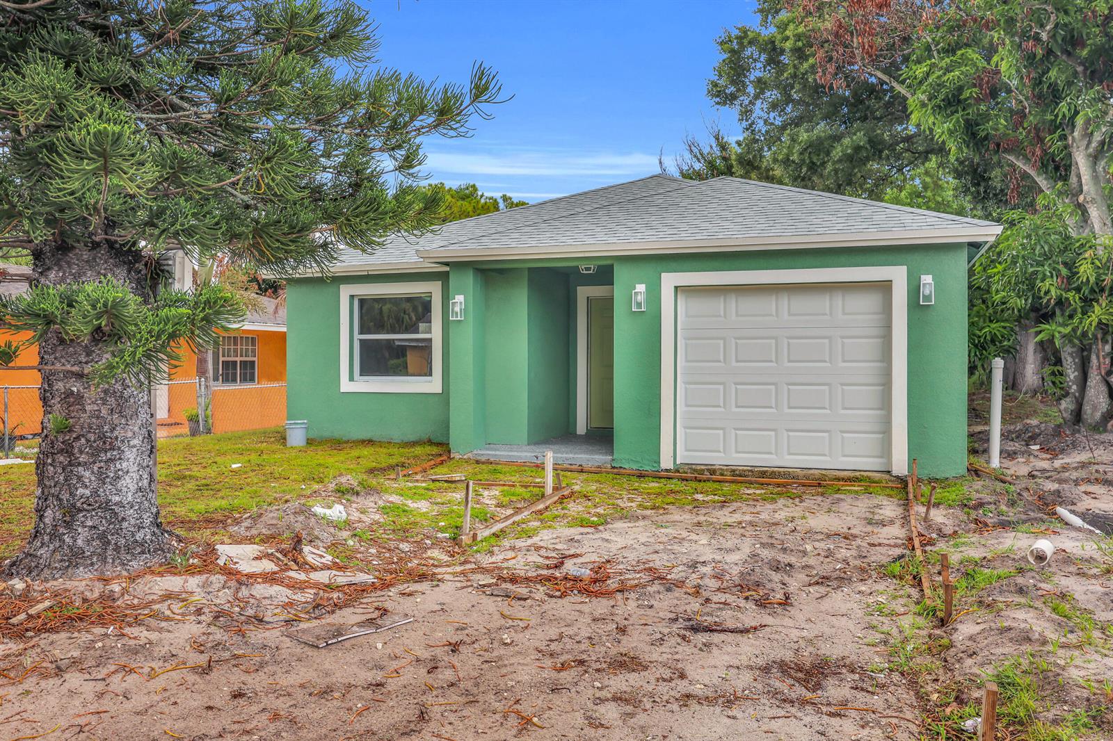 A green single-story house with a white garage door and a dirt front yard — 2002 Avenue M, Fort Pierce FL 34950, FORT PIERCE, FL