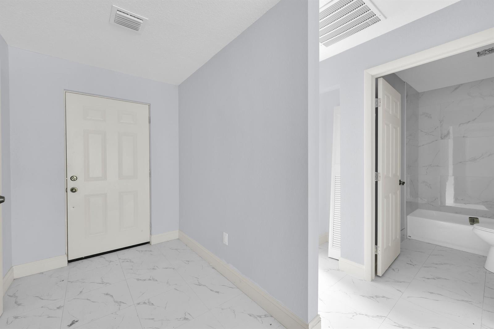 A white door opens into a tiled entryway next to a bathroom with marble flooring — 2002 Avenue M, Fort Pierce FL 34950, FORT PIERCE, FL