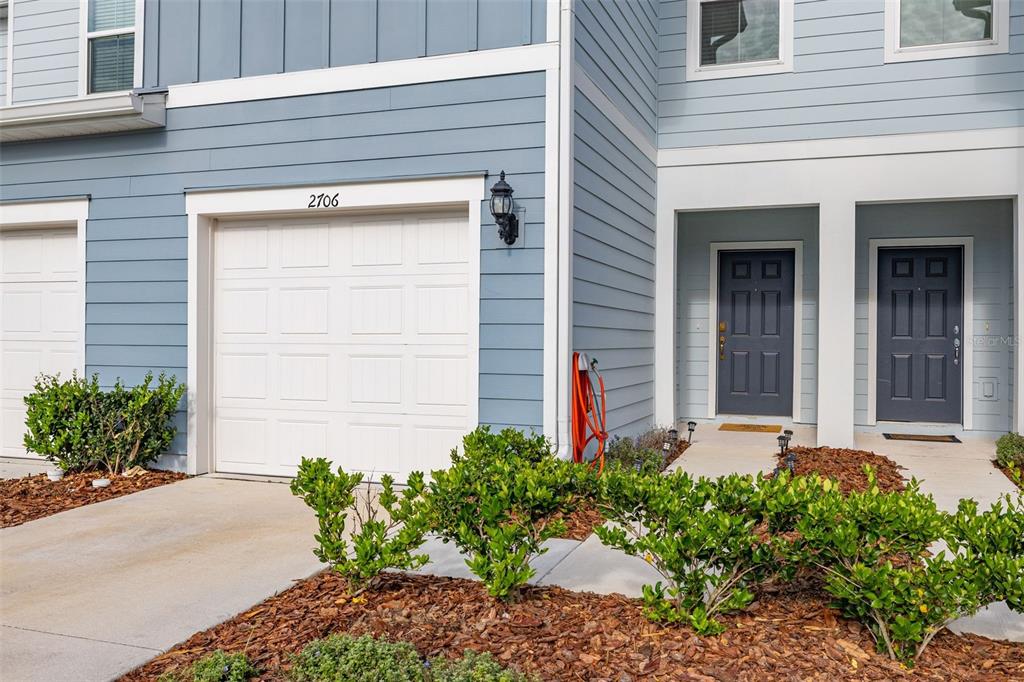 A blue-sided townhouse exterior features a white garage door, two front doors, and landscaping — 2706 FETCHING TRAIL, DAVENPORT, FL