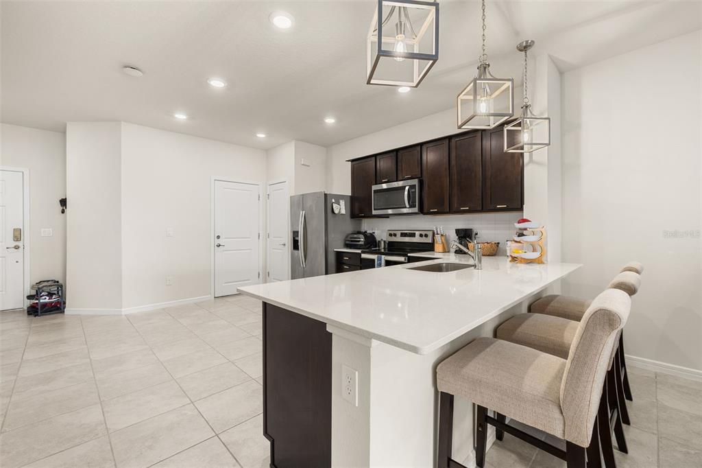 A kitchen features dark wood cabinets, white countertops, a central island, and three bar stools — 2706 FETCHING TRAIL, DAVENPORT, FL