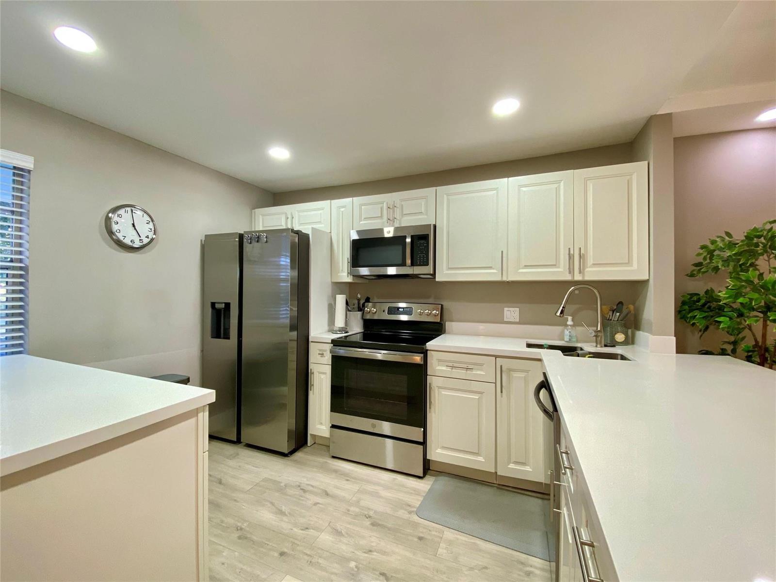 A kitchen features white cabinets, stainless steel appliances, and light-colored countertops — 3010 N Course Drive # 209, Pompano Beach FL 33069, POMPANO BEACH, FL