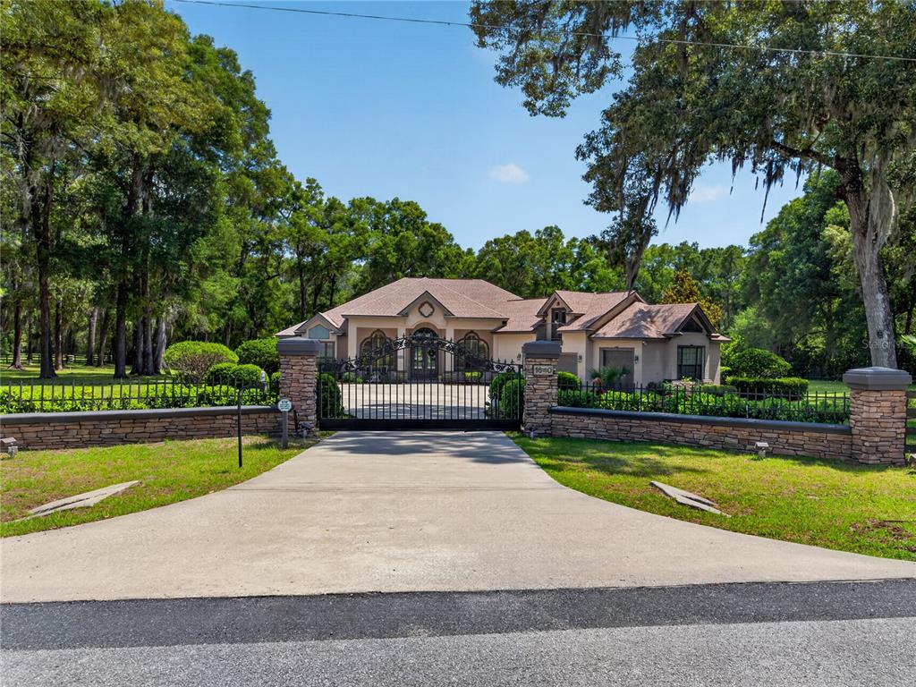 A gated driveway leads to a single-story house with a stone wall and mature trees — 1640 SE 91ST PLACE, OCALA, FL