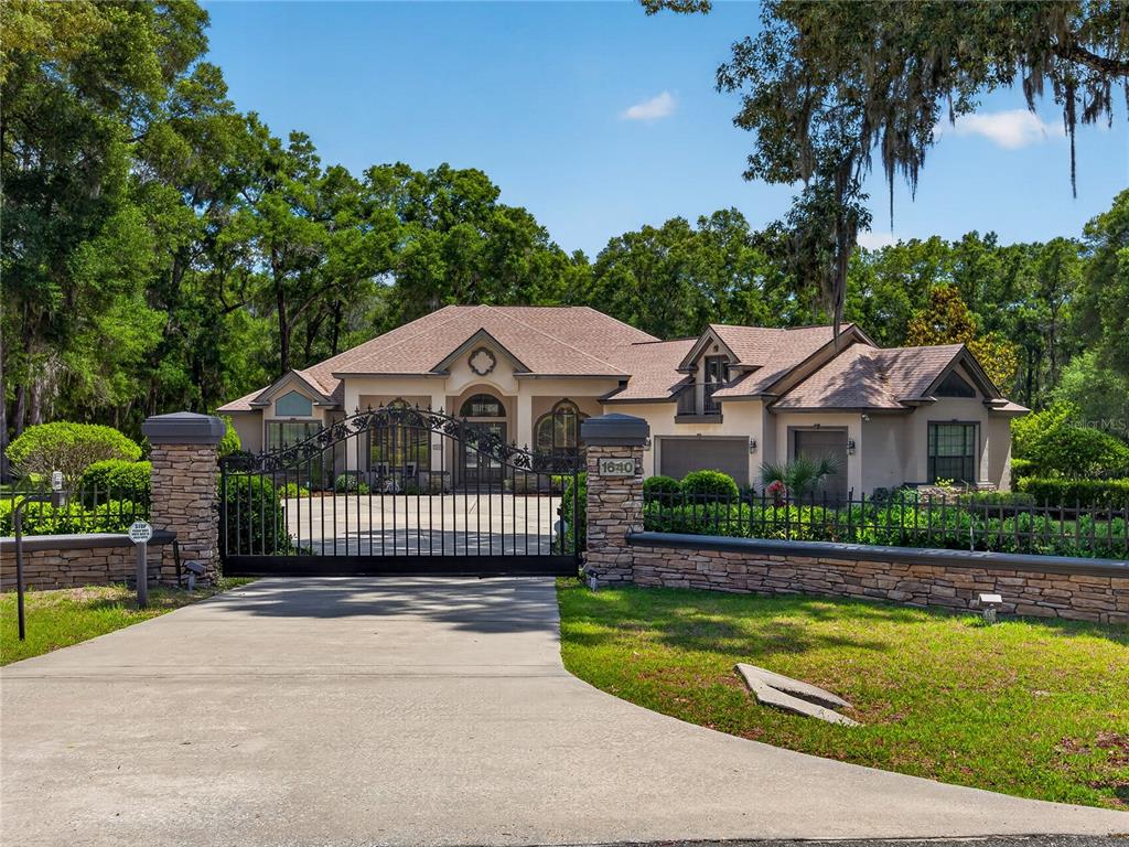 A single-story house with a gated driveway and stone wall sits behind a lush lawn — 1640 SE 91ST PLACE, OCALA, FL