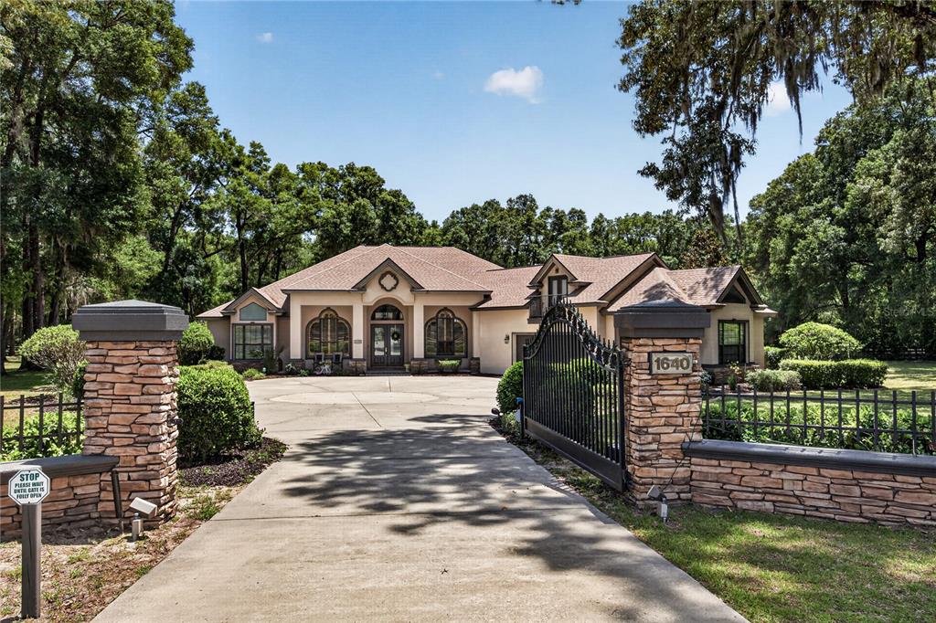 A gated driveway leads to a single-story house with a stone-accented entrance and roof gables — 1640 SE 91ST PLACE, OCALA, FL